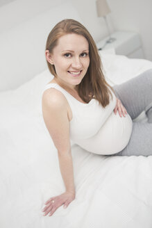 Porträt einer lächelnden schwangeren Frau auf dem Bett - VTF000505