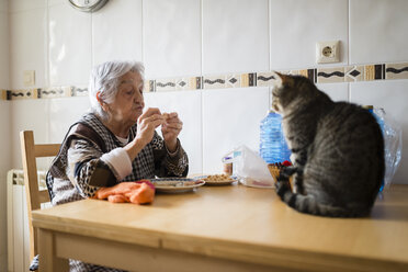 Senior woman eating while the cat watching her - RAEF000820