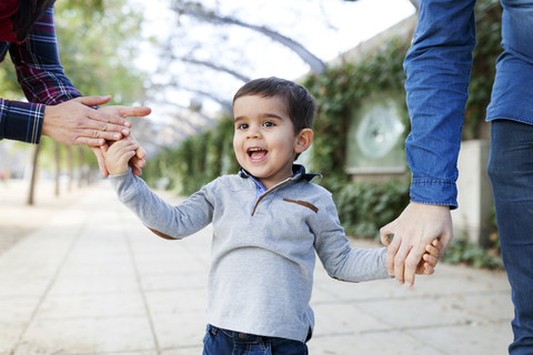 Porträt eines glücklichen Kleinkindes, das Hand in Hand mit seinen Eltern geht, lizenzfreies Stockfoto