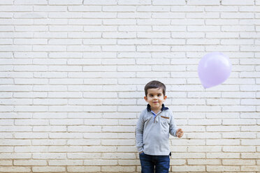 Portrait of toddler standing in front of white wall holding a balloon - VABF000110