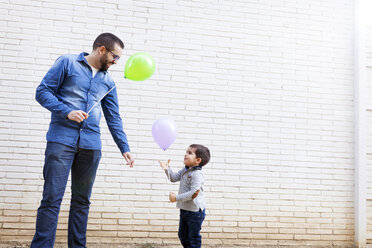 Vater und sein kleiner Sohn mit Luftballons vor einer weißen Backsteinmauer - VABF000111