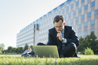 Businessman sitting on meadow using laptop - JUBF000088