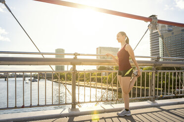 Germany, Frankfurt, young athlete stretching on bridge - PUF000468