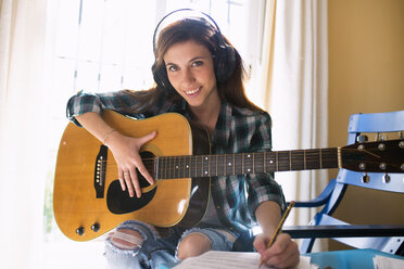 Smiling young woman with headphones, guitar and music sheet - KIJF000135