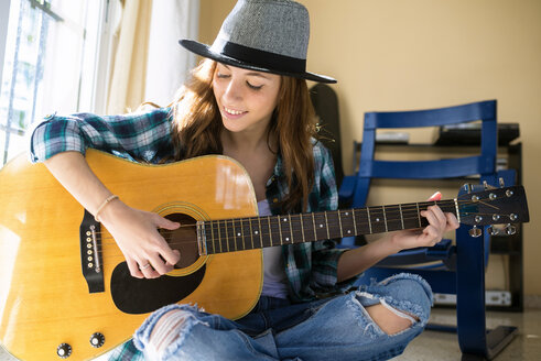 Lächelnde junge Frau spielt drinnen Gitarre - KIJF000140