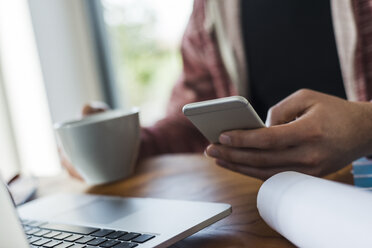 Close-up of man with cell phone and laptop at desk - UUF006366