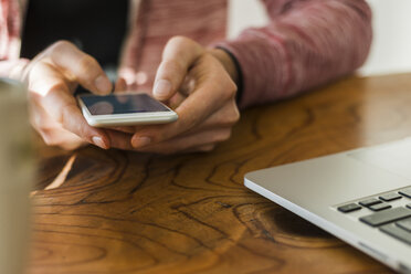 Nahaufnahme eines Mannes mit Mobiltelefon und Laptop am Schreibtisch - UUF006368