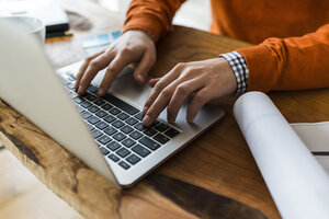 Nahaufnahme eines Mannes mit Laptop neben einem Bauplan am Schreibtisch - UUF006373