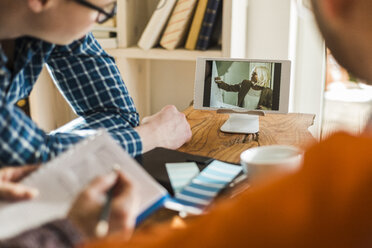 Colleagues at desk watching video film on digital tablet - UUF006379