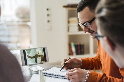 Kollegen diskutieren im Büro mit Videofilm auf digitalem Tablet im Hintergrund - UUF006391