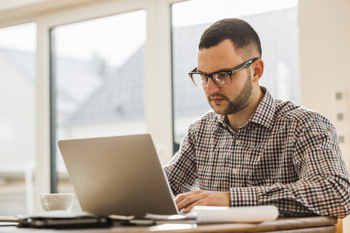 Junger Mann mit Laptop am Schreibtisch - UUF006410