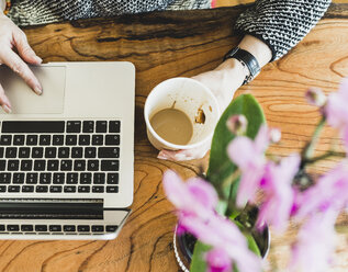 Nahaufnahme einer Frau mit Kaffee und Laptop am Schreibtisch - UUF006422