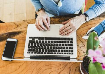 Close-up of woman with smartphone and laptop at desk - UUF006423