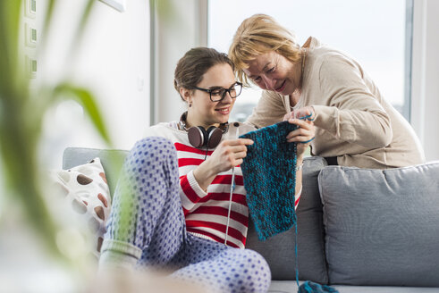 Junge Frau sitzt auf einer Couch und zeigt einer älteren Frau Strickwaren - UUF006438