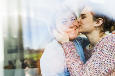 Young woman kissing senior woman behind windowpane - UUF006449