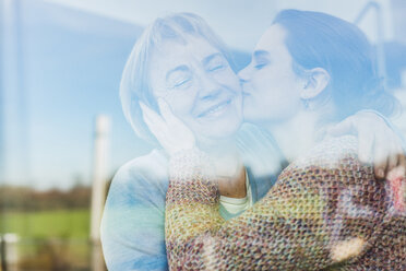 Young woman kissing senior woman behind windowpane - UUF006451