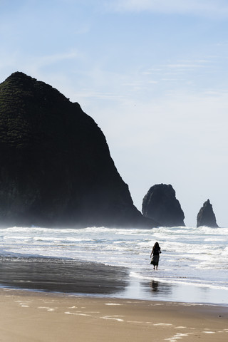 USA, Oregon, Cannon Beach, Haystack Rock, Frau am Strand, lizenzfreies Stockfoto
