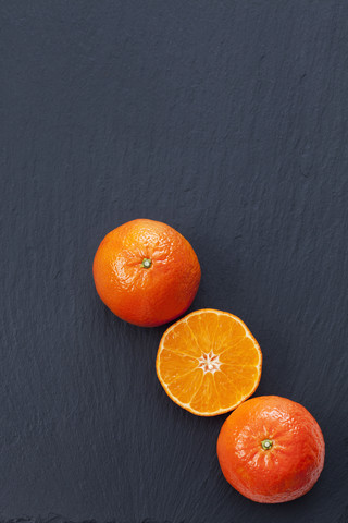 Ganze und in Scheiben geschnittene Mandarinen auf Schiefer, lizenzfreies Stockfoto
