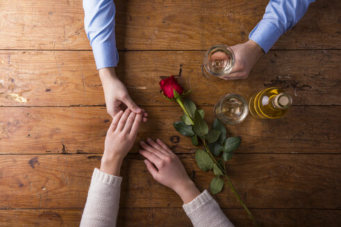 Hände eines jungen Paares mit roter Rose und einer Flasche Weißwein - HAPF000174