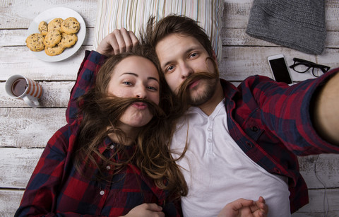 Portrait of young couple lying on the floor taking a selfie stock photo