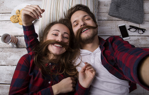 Portrait of young couple lying on the floor taking a selfie stock photo