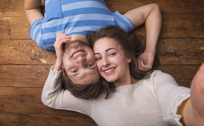 Portrait of young couple in love lying head to head on wooden floor - HAPF000194