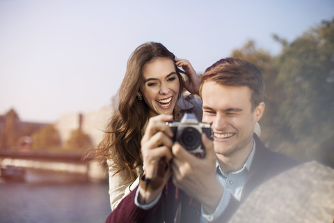 Germany, Berlin, happy young couple with camera at bank of River Spree stock photo