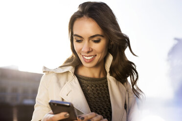 Lächelnde junge Frau hält Smartphone im Freien - GCF000167