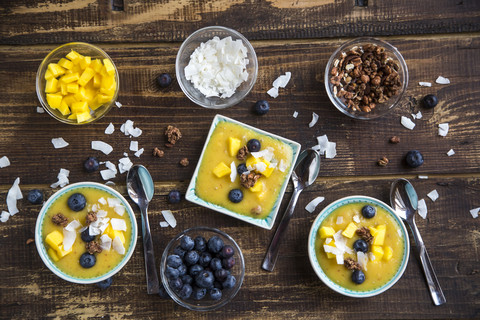 Schalen mit Mango-Smoothie mit Mangowürfeln, Kokosraspeln, Blaubeeren und Schoko-Crunch, lizenzfreies Stockfoto