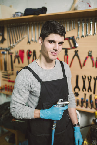 Porträt eines Mechanikers in seiner Werkstatt mit einer Kompressorpistole, lizenzfreies Stockfoto