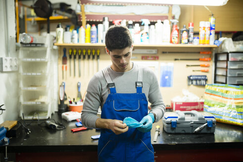 Mechaniker in seiner Werkstatt beim Anziehen von Arbeitshandschuhen - RAEF000833