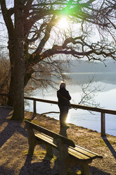 Germany, Bavaria, Lake Staffelsee, senior woman at lakeshore in backlight - LAF001601