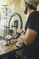 Mechaniker bei der Arbeit an einem Reifen in einem Geschäft für maßgeschneiderte Fahrräder - JUBF000106