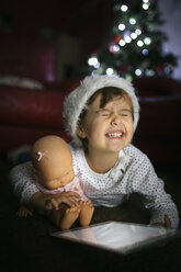 Porträt eines kleinen Mädchens mit Weihnachtsmütze, digitalem Tablet und Puppe zu Hause - MGOF001332