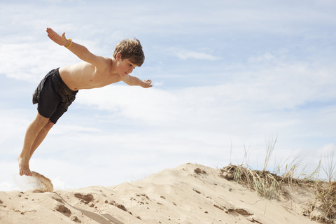 Sweden, Mellby, boy on beach dune jumping into the air with outstretched arms stock photo
