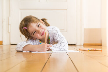 Portrait of smiling little girl lying on wooden floor with crayons and sheet of paper - LVF004509