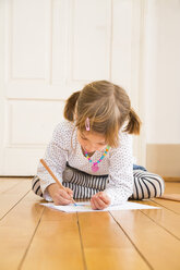 Little girl sitting on wooden floor painting with crayon - LVF004511