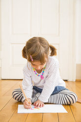 Little girl sitting on wooden floor painting with crayon - LVF004512