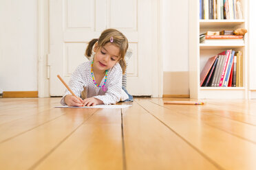 Portrait of smiling little girl lying on wooden floor painting with crayons - LVF004513