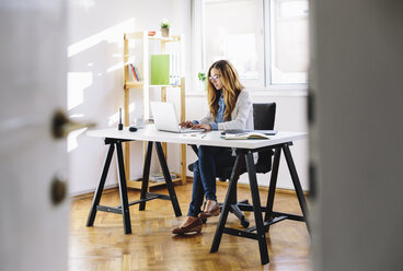 Young woman working with laptop at home office - AKNF000035