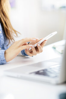 Hands of young woman using smartphone at desk in the office - AKNF000039