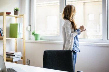 Young woman taking a rest with cup of coffee at her home office - AKNF000043