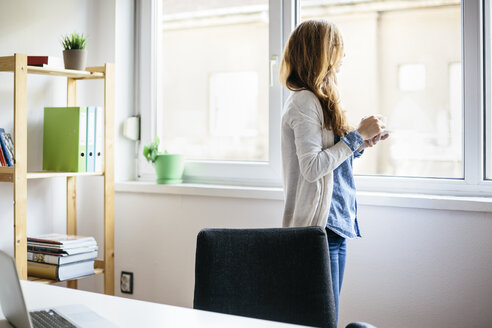 Junge Frau ruht sich mit einer Tasse Kaffee in ihrem Büro zu Hause aus - AKNF000043