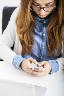 Young woman using her smartphone at desk in the office - AKNF000044