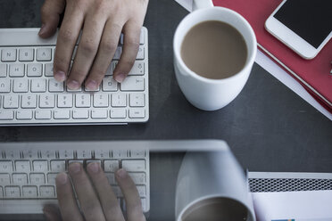 Nahaufnahme eines Mannes bei der Arbeit am Computer neben einer Kaffeetasse - ZEF008338