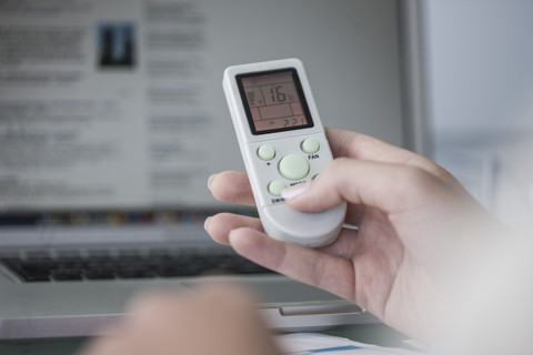 Nahaufnahme einer Frau mit einer Fernbedienung für eine Klimaanlage, lizenzfreies Stockfoto