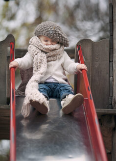 Portrait of little girl wearing big scarf and woolly hat on a slide - NIF000074