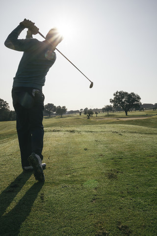 Hintergrundbeleuchtung eines Golfspielers, der einen Golfball auf einem Golfplatz abschlägt, lizenzfreies Stockfoto