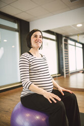 Schwangere Frau macht Pilates-Übungen mit Gymnastikball in einem Fitnessstudio - RAEF000836