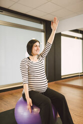 Pregnant woman doing Pilates exercises with gym ball in a gym - RAEF000839